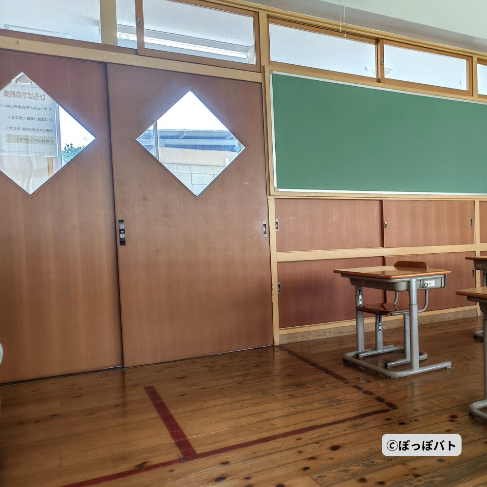 旧小見野小学校の教室内にある菱形の窓付き扉と机